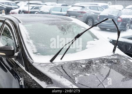 Close-up detail view of black modern car with raised up windshield wiper blades to prevent icing in cold frost winter day. Vehicle windscreen covered Stock Photo