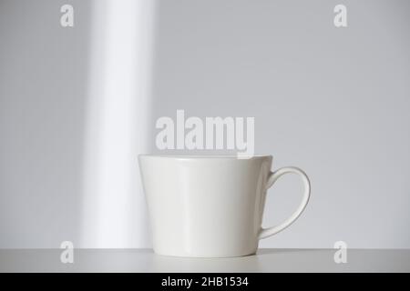 white cup on white background with ray of sun. Morning self-care routine minimalism and getting ready. Front view Stock Photo