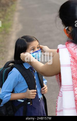 An Indian school girl child going to school again after pandemic with her mother wearing nose mask protection Stock Photo