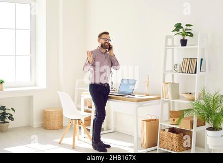 Excited male entrepreneur making business call working remotely from his home office. Stock Photo