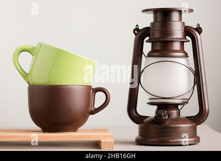 two brown and green cups of coffee or tea on wood with lamp and white background Stock Photo