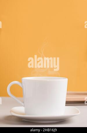 white mug with hot drink, coffee or tea, with orange-yellow background Stock Photo