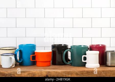Multicolored mugs on a wooden kitchen board in front of a subway tiles wall Stock Photo