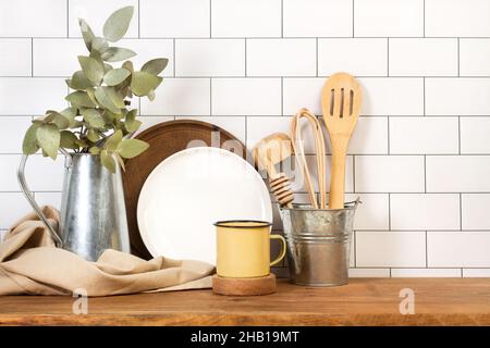Metal mug and kitchen utensils on a wooden board in front of a subway tiles wall Stock Photo