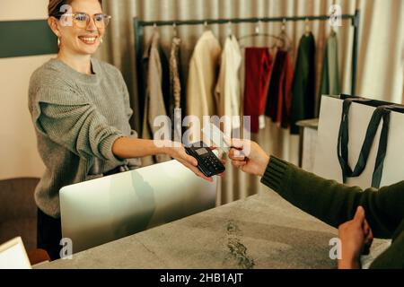 Friendly store assistant taking a card payment from a female customer. Happy shop assistant helping a female customer while standing behind the counte Stock Photo