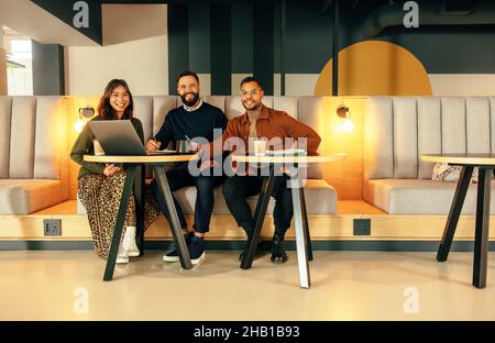 Happy businesspeople working in a modern office lobby. Team of happy businesspeople smiling at the camera while sitting on a couch. Group of entrepren Stock Photo