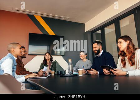 Cheerful businesspeople having a meeting in a boardroom. Group of multiethnic businesspeople smiling happily during their morning briefing. Young entr Stock Photo