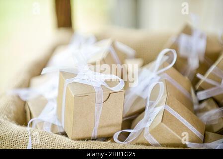 Miniature  brown cardboard gift boxes wrapped with white bows and laces inside of canvass basket Stock Photo