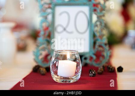 Glass candle holder with white lit candle centerpiece on red table cloth wedding reception Stock Photo