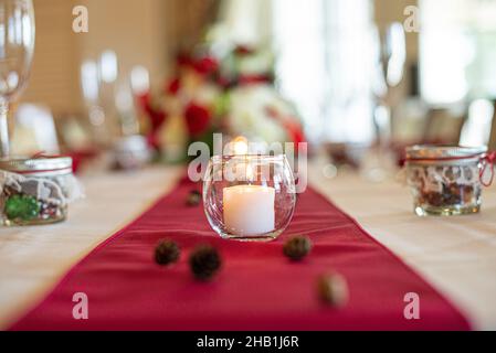 Glass candle holder with white lit candle centerpiece on red table cloth wedding reception Stock Photo