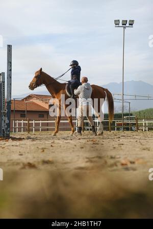Trainer teaching kid horse back riding with obstacles. Stock Photo