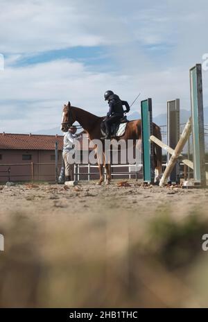 Trainer teaching kid horse back riding with obstacles. Stock Photo