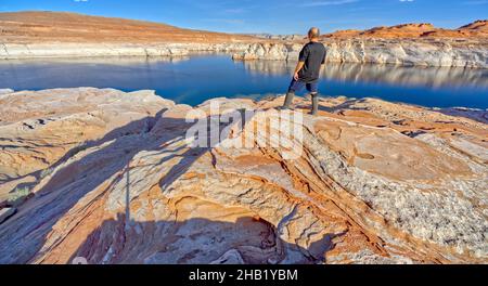 A man hiking near the rocky shoreline of Lake Powell in an area called the Chains in the Glen Canyon Recreation Area of Page Arizona. Stock Photo