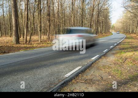 A car driving fast on an asphalt road through the forest, autumn view Stock Photo