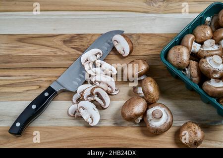 Fresh Baby Bella Mushrooms being sliced on wood kitchen countertop Stock Photo