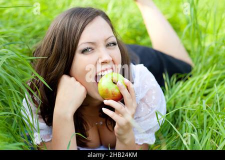 Apple, lying, woman, meadow, bite, bite, teeth, face, apple, bite, red, Styria, person, laughing, one, Austria, leisure, looking, Leibnitz, blouse, gr Stock Photo