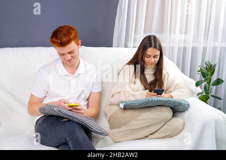 Young couple relaxing and spending time together on the couch while staying at home using smart phones. Stock Photo