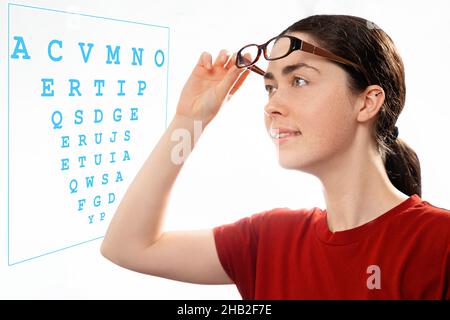 Ophthalmology. Portrait of a young beautiful woman taking off her glasses and looking at a diagram to check her vision. The concept of healthy eyes an Stock Photo