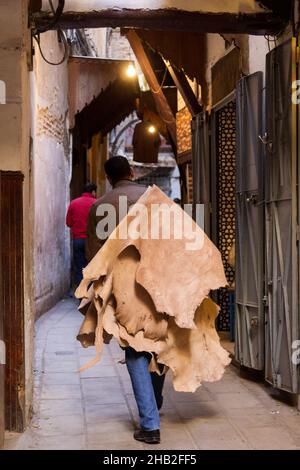 Fez, Morocco  - February 23. 2019: Local people carrying raw leather on back through the narrow lane in medina (old town center) to the market near th