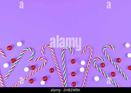 Christmas candy canes and ornament balls at bottom of purple background with copy space Stock Photo