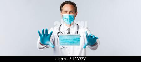 Covid-19, virus, healthcare workers and vaccination concept. Doctor in PPE extend hands and give patient medical mask, recommend using preventing Stock Photo