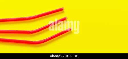 Three pink plastic drinking straws on yellow board, view from above Stock Photo