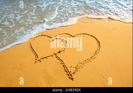 Two hearts handwritten on sand of tropical beach, background Stock Photo