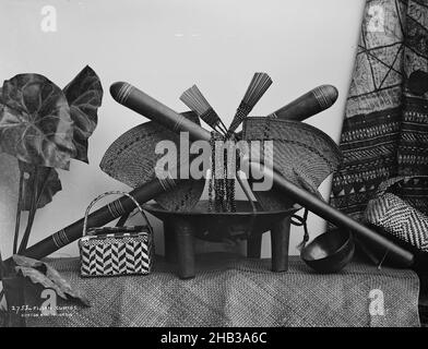 Fijian Curios, Burton Brothers studio, photography studio, circa 1884, Dunedin, black-and-white photography, Studio set up of a kava bowl, kava cup and weaved basket on top of a weaved mat, above two fans, two hair combs, necklaces and two clubs that cross over each other. Left is a tropical plant, right is a tapa cloth Stock Photo