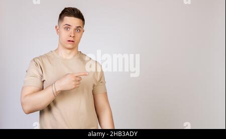 The man the guy points to the side with a displeased face. Young doubter man, holds his hand and points to the side with forefingers at blank space. Stock Photo