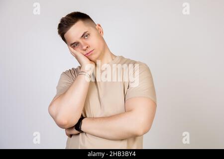 Young handsome guy holding his head with his hand, tired after a long and hard working day, standing on a white background looking at the camera Stock Photo
