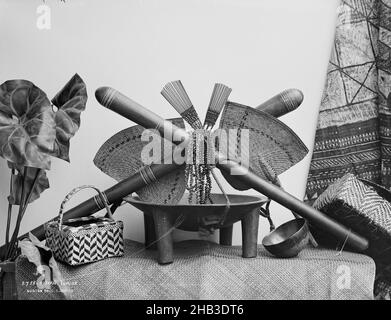 Fijian Curios, Burton Brothers studio, photography studio, circa 1884, Dunedin, black-and-white photography, Studio set up of a kava bowl, kava cup and weaved basket on top of a weaved mat, above two fans, two hair combs, necklaces and two clubs that cross over each other. Left is a tropical plant, right is a tapa cloth Stock Photo