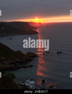 landscape of an orange sunset over the horizon of the sea, the rays pass through the cliff reflecting in the sea Stock Photo