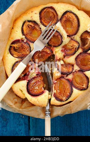 Plum cake in bake paper with two forks on blue background vertical Stock Photo
