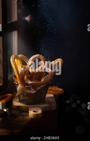 Traditional Spanish churros on the table. Dark and moody photo, rustic style. Magic light goes from the window Stock Photo