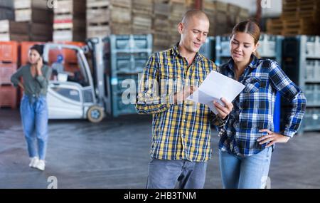Female manager discussing order list with male worker at warehouse Stock Photo