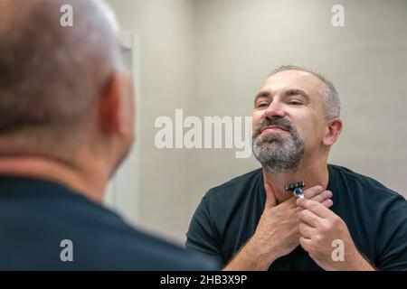 Serious handsome man looking in mirror and shaving his whiskers Stock Photo