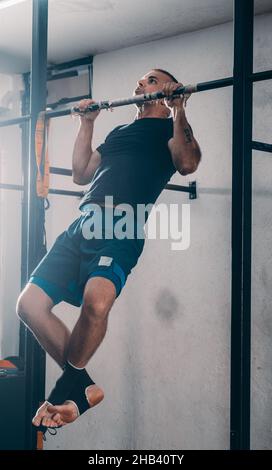 Crossfit man doing pull-ups on chin-up bar during workout outdoors Stock Photo