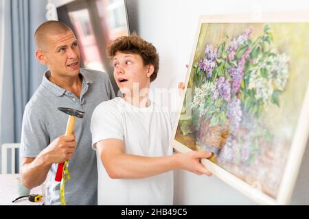 Son helps father to hang the painting on the wall of house Stock Photo