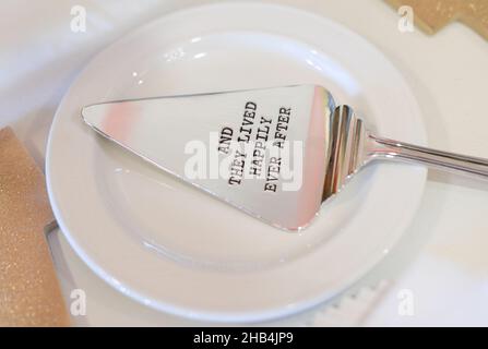 Silver cake serving utensil engraved with the phrase 'You are my greatest adventure' on white plate at wedding reception cake table Stock Photo