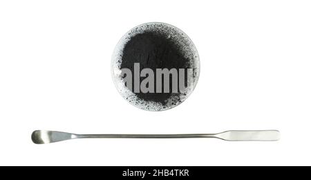 Carbon Charcoal Powder in Chemical Watch Glass placed next to the stainless spatula. Close up chemical ingredient on white laboratory table. Top View Stock Photo