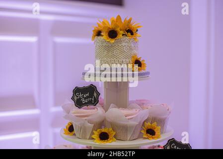 Beautiful  wedding cake decorated with lace and sunflowers at the top of cupcake tower Stock Photo