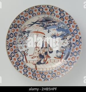 Dish with a woman and attendant on a bridge in a landscape, Dish of porcelain, painted in underglaze blue and on the glaze red and gold. On the plate and wall in a medallion a woman on a bridge, behind her a servant with a parasol. In the background a river landscape with boats, on the bank pavilions, people and trees. The border with a honeycomb pattern filled with flowers. The reverse with six flower branches (prunus). Seven thick pros on the underside. Imari., anonymous, Japan, c. 1675 - c. 1699, porcelain, glaze, painting, gilding, vitrification, height 23.3 cm, diameter 7.7 cm, diameter Stock Photo
