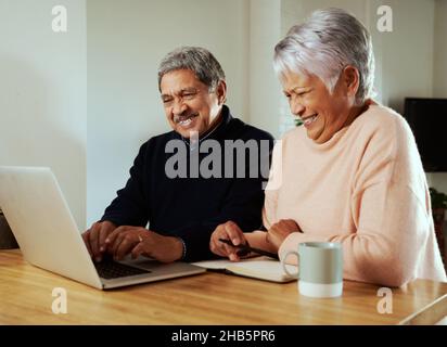 Multi-cultural elderly couple smiling at family on online call. Sitting at modern kitchen counter with laptop. Stock Photo