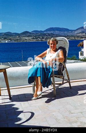 Middle aged female tourist sitting in sun on terrace by the sea, island of Ibiza, Balearic Islands, Spain, 1950s Stock Photo