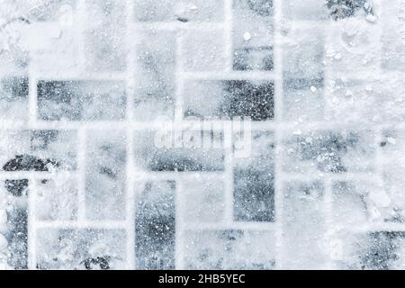 Top aboe overhead view of stone slab tiled pavement covered with snow cold winter day. Footprints on slippery surface. Weather forecast. Abstract Stock Photo