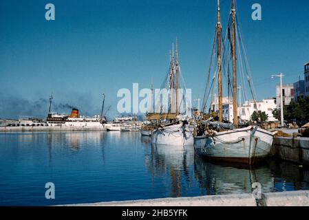 Traditional wooden sailing ships in harbour with funnel of ferry ship in background, San Antonio, island of Ibiza, Balearic Islands, Spain, 1950s Stock Photo