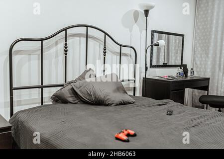 teenager's room in nondescript gray tones with crumpled linens on bed and game joystick, floor lamp and a desk. Gamer room, teen room interior Stock Photo