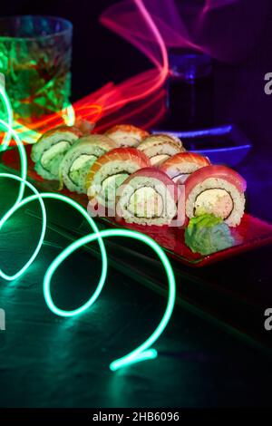Set of sushi rolls and glass of beverage on bar counter with bright colorful LED strip lighting Stock Photo