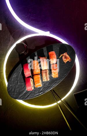 Assorted rolls with salmon, tuna, eel and shrimp on black background with neon LED light strip Stock Photo