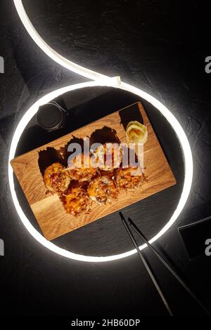 Fried sushi rolls with melted cheese and bonito flakes on black background with LED strip Stock Photo